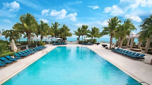 Ein Swimmingpool mit Liegestühlen und Palmen, umgeben von einem Gebäude mit Blick aufs Meer.
