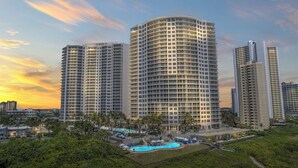 Ein Hochhotel mit mehreren Balkonen, einem Schwimmbecken und üppiger Bepflanzung.