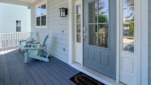 A porch with two Adirondack chairs, a grey door, and a welcome mat. - Heated Pool Access | 5*Clean | Flex Cancelation (Tybee Island)