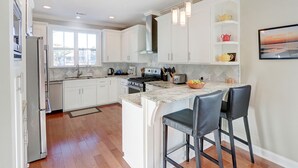 A modern kitchen with white cabinetry, a marble island, and bar stools. - Heated Pool Access | 5*Clean | Flex Cancelation (Tybee Island)