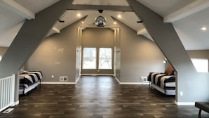 A spacious attic bedroom with a sloped ceiling, large windows, and a chandelier.