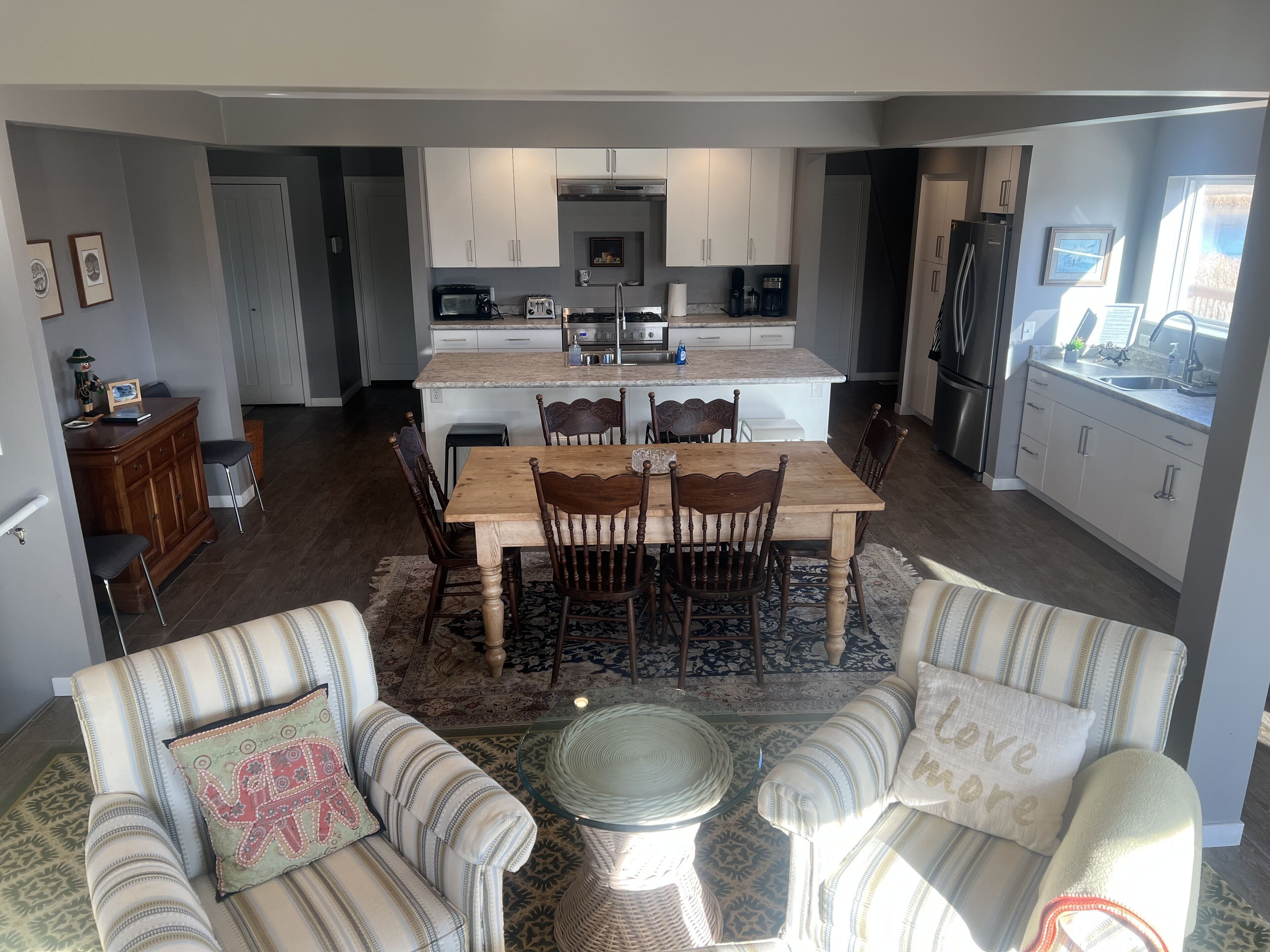 A modern kitchen with white cabinets, a central island, and a dining area with wooden chairs.