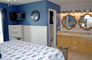 Une chambre à coucher comprenant un lit, une télévision, un miroir rond, ainsi qu’une salle de bain avec un lavabo et un meuble-lavabo.