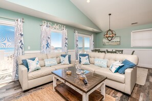 A living room with a sectional sofa, a coffee table, and a view of the beach.