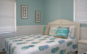 Un dormitorio con una cama, dos relojes de pared y una almohada con motivos playeros.