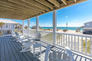 A wooden deck with white rocking chairs and a view of the beach.