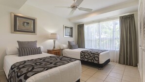 A hotel room with two beds, a ceiling fan, a window with curtains, and framed pictures on the wall.