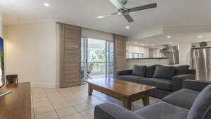 A modern living room with a sofa, coffee table, and a ceiling fan. There is a sliding glass door leading to a balcony with outdoor furniture.