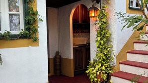 A building entrance with a red-tiled floor, a white and yellow facade, and a wooden staircase.
