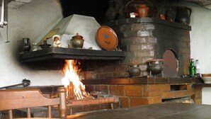 A traditional brick fireplace with a fire burning, surrounded by various ceramic pots and a shelf with decorative items.