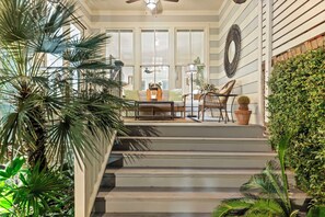 A covered porch with a sofa and chairs, surrounded by potted plants and a staircase. - Heated Pool Access | 5*Clean | Flex Cancelation (Savannah)