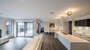 Et moderne køkken med en central ø, et spiseområde med hvide stole og et stort vindue med udsigt til en baghave.