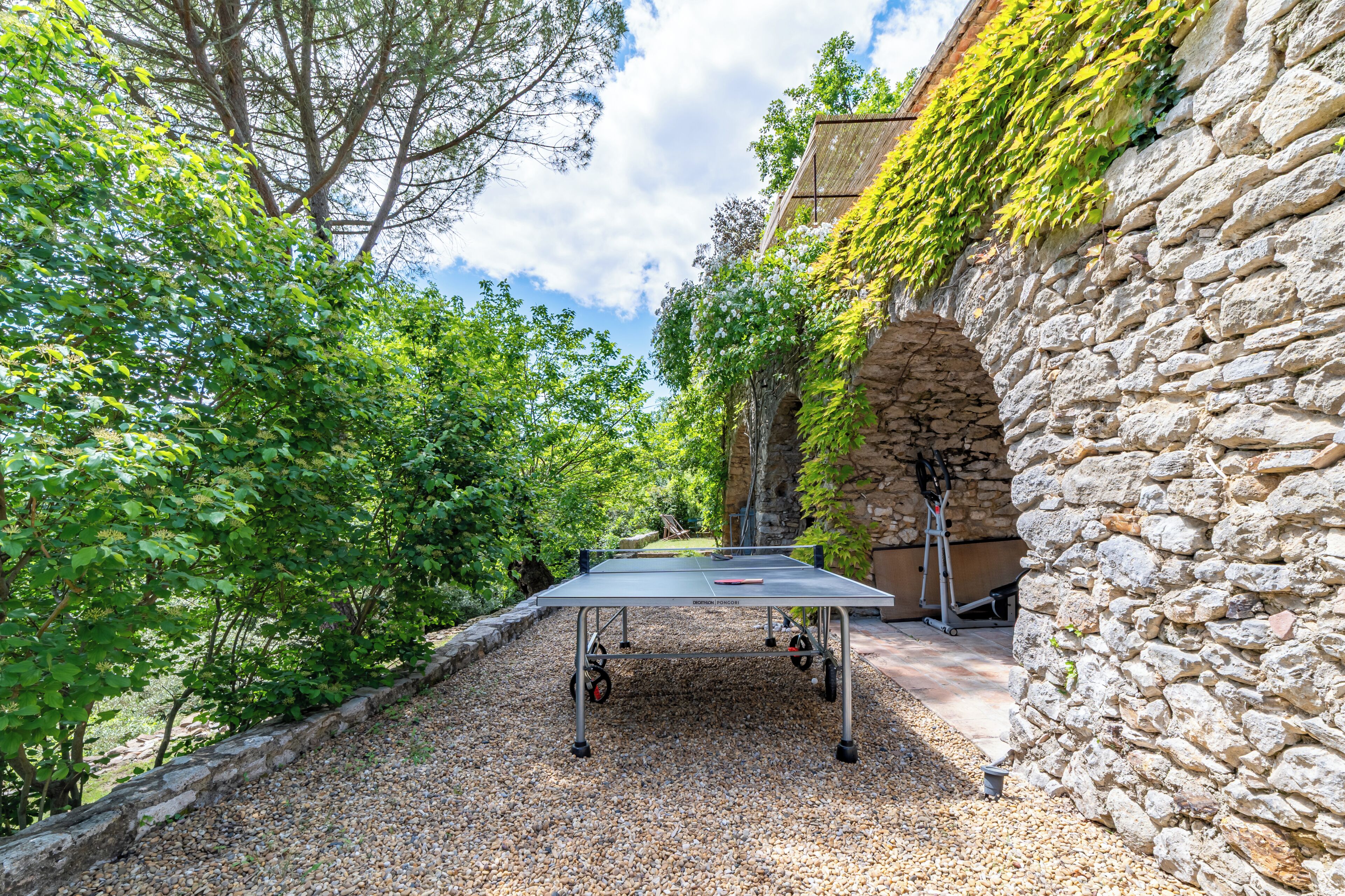 Una mesa de ping pong en un patio con paredes de piedra y vegetación.