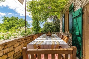 An outdoor dining area with a stone wall, wooden benches, and a table with a striped tablecloth.