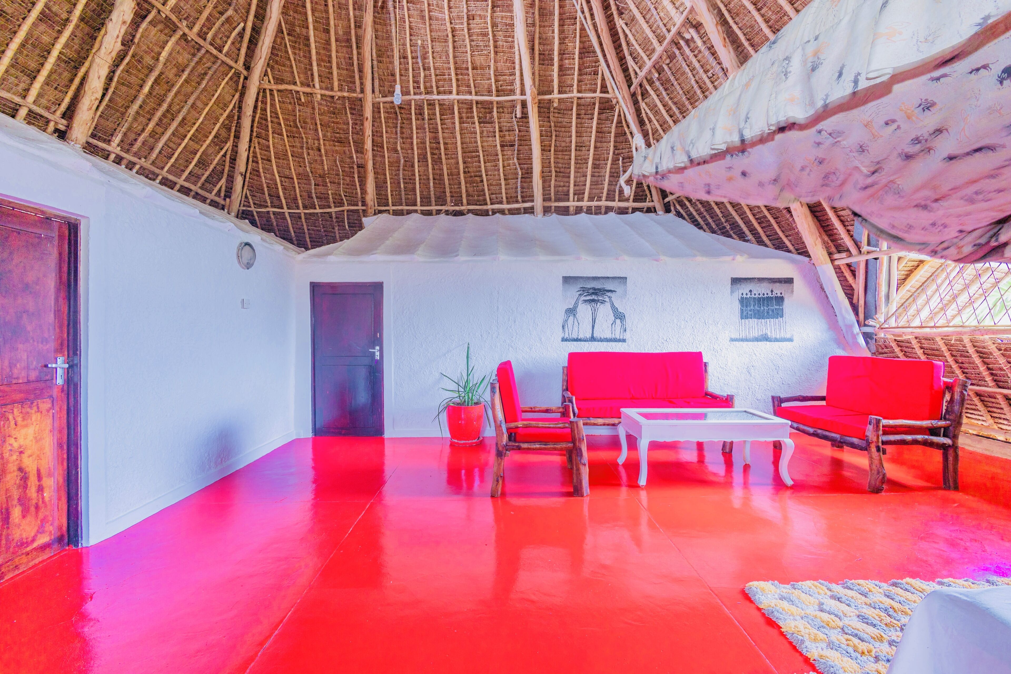 Una habitación con piso rojo, muebles de madera y techo de paja.