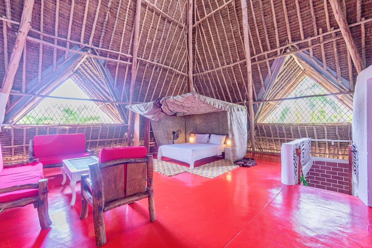 A room with a high ceiling, a bed, a red sofa, and a small table.