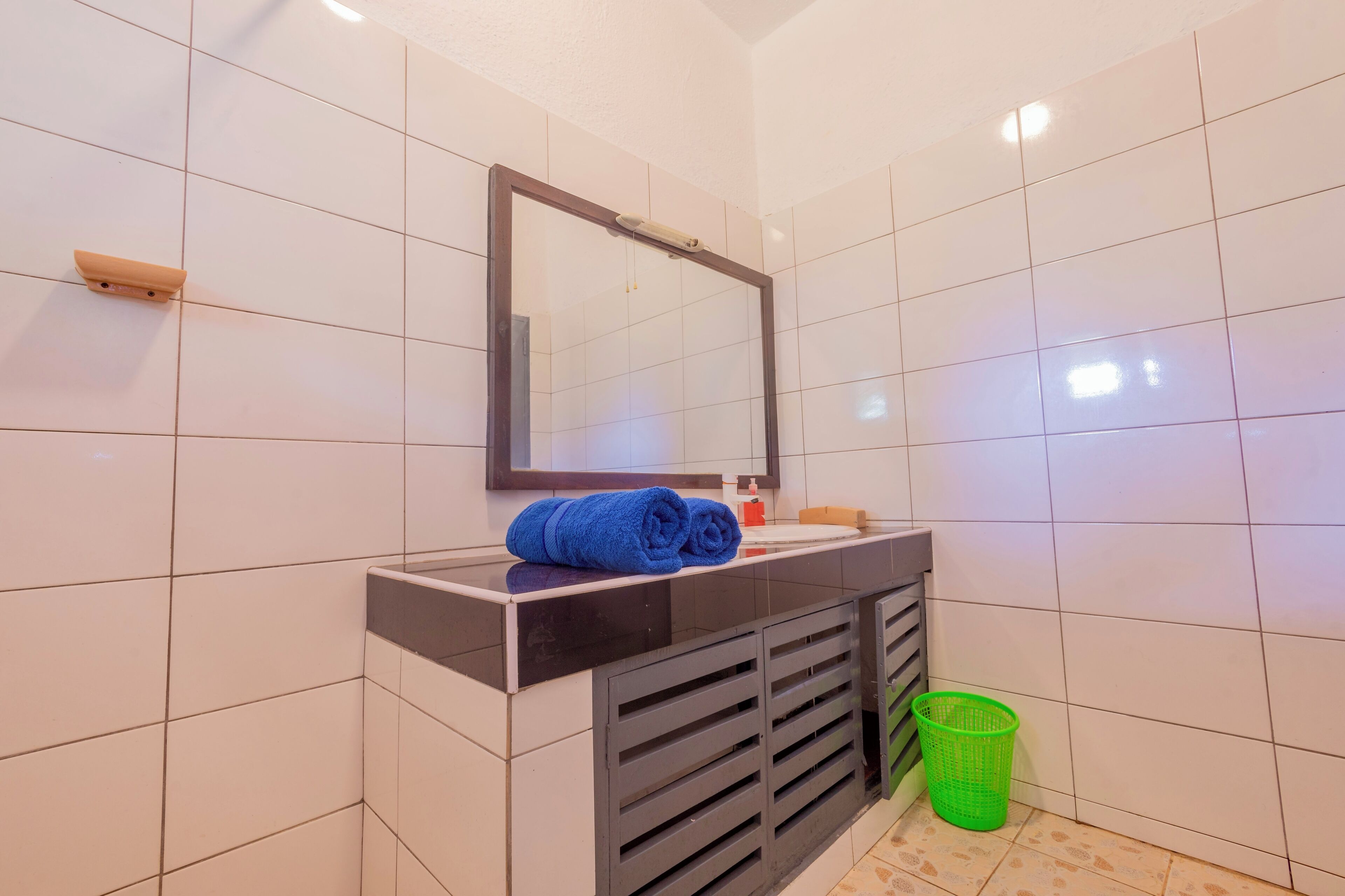 A bathroom with white tiled walls, a black vanity with a mirror, and a green basket.