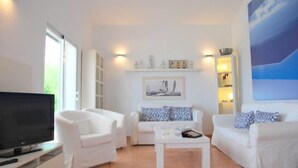 A modern living room with white furniture, a flat-screen TV, and a painting on the wall.