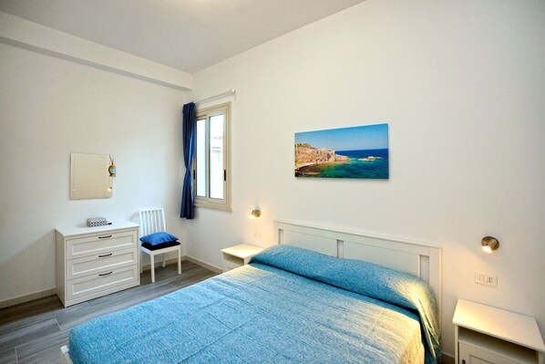 A bedroom with a bed, a chair, a desk, and a painting on the wall.