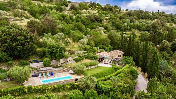 A hillside villa with a swimming pool, stone walls, and lush greenery.