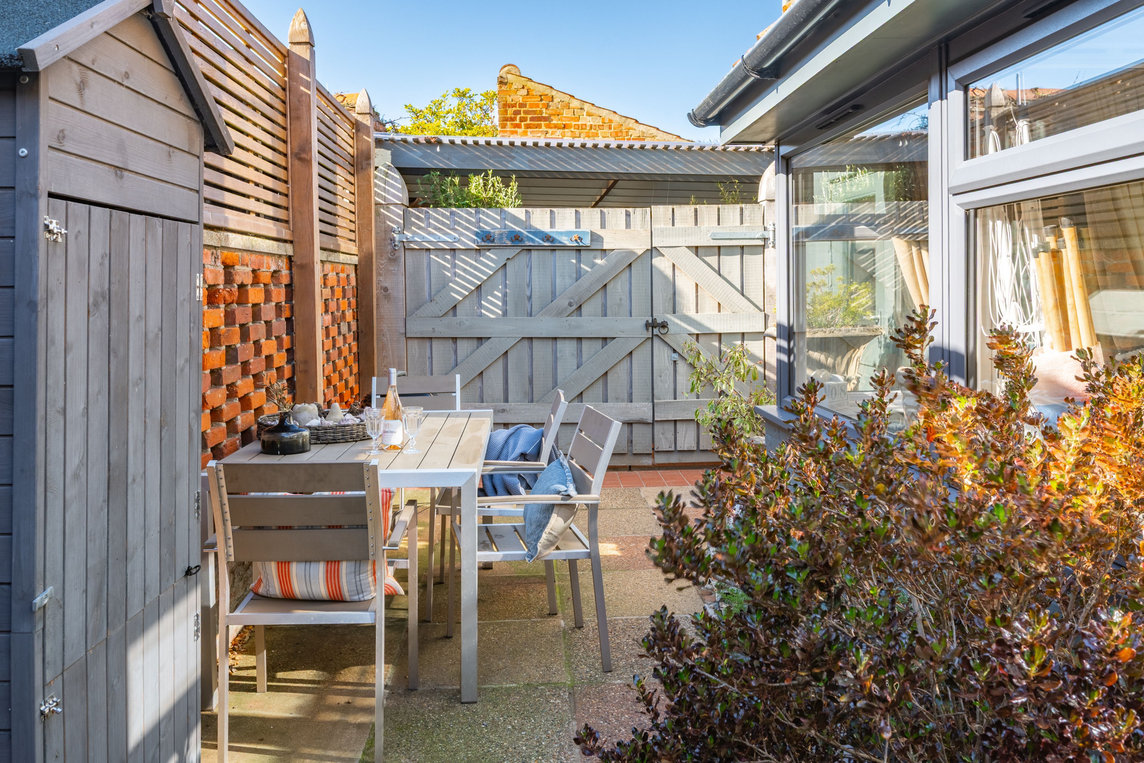 A patio with a table and chairs, a wooden fence, and a view of a brick wall.