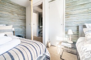A bedroom with a bed, bedside tables, a lamp, and a view of a staircase.
