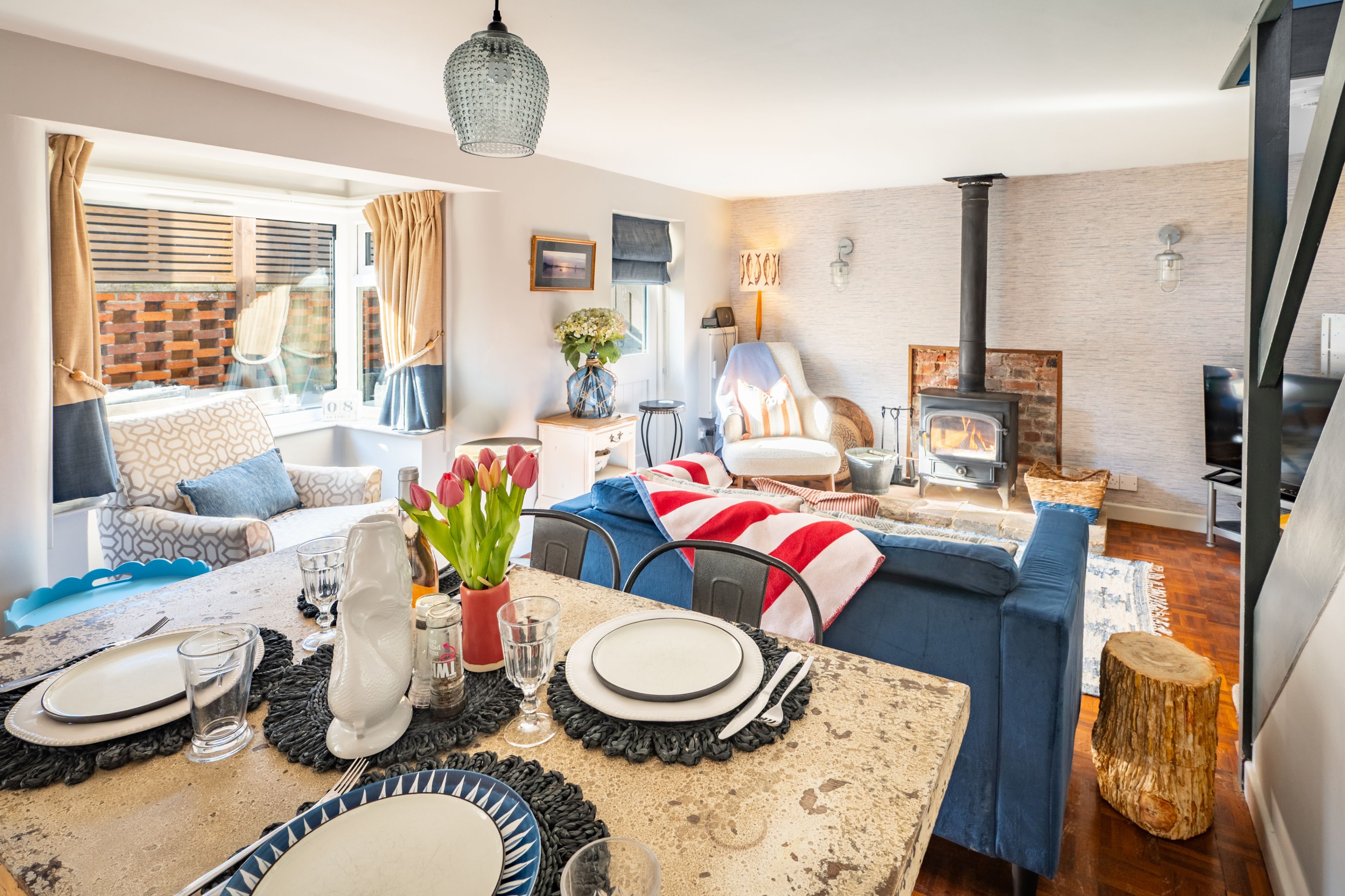 A modern living room with a fireplace, a dining area with a table set for four, and a cozy seating area with a sofa and armchairs.