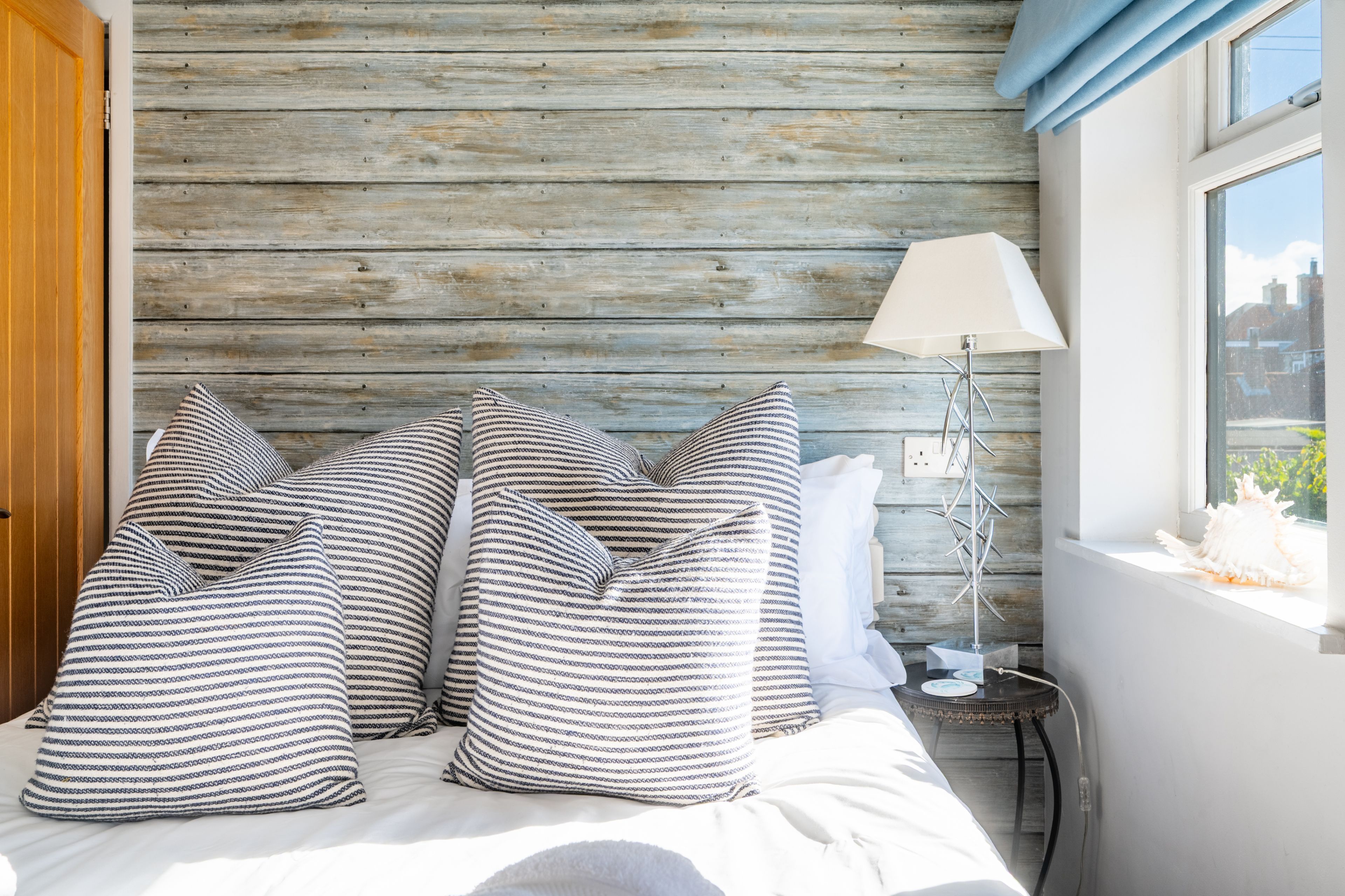 Ein Bett mit gestreiften Kissen, eine Lampe und ein Blick nach draußen durch ein Fenster.