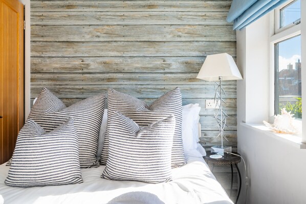 A bed with striped pillows, a lamp, and a view of the outside through a window. - Hillview Lodge, Brancaster Staithe, Norfolk (Brancaster Staithe)