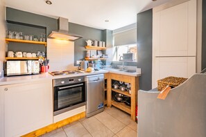 A compact kitchen with a stove, oven, and dishwasher. There are wooden shelves above the counter holding various kitchen items.