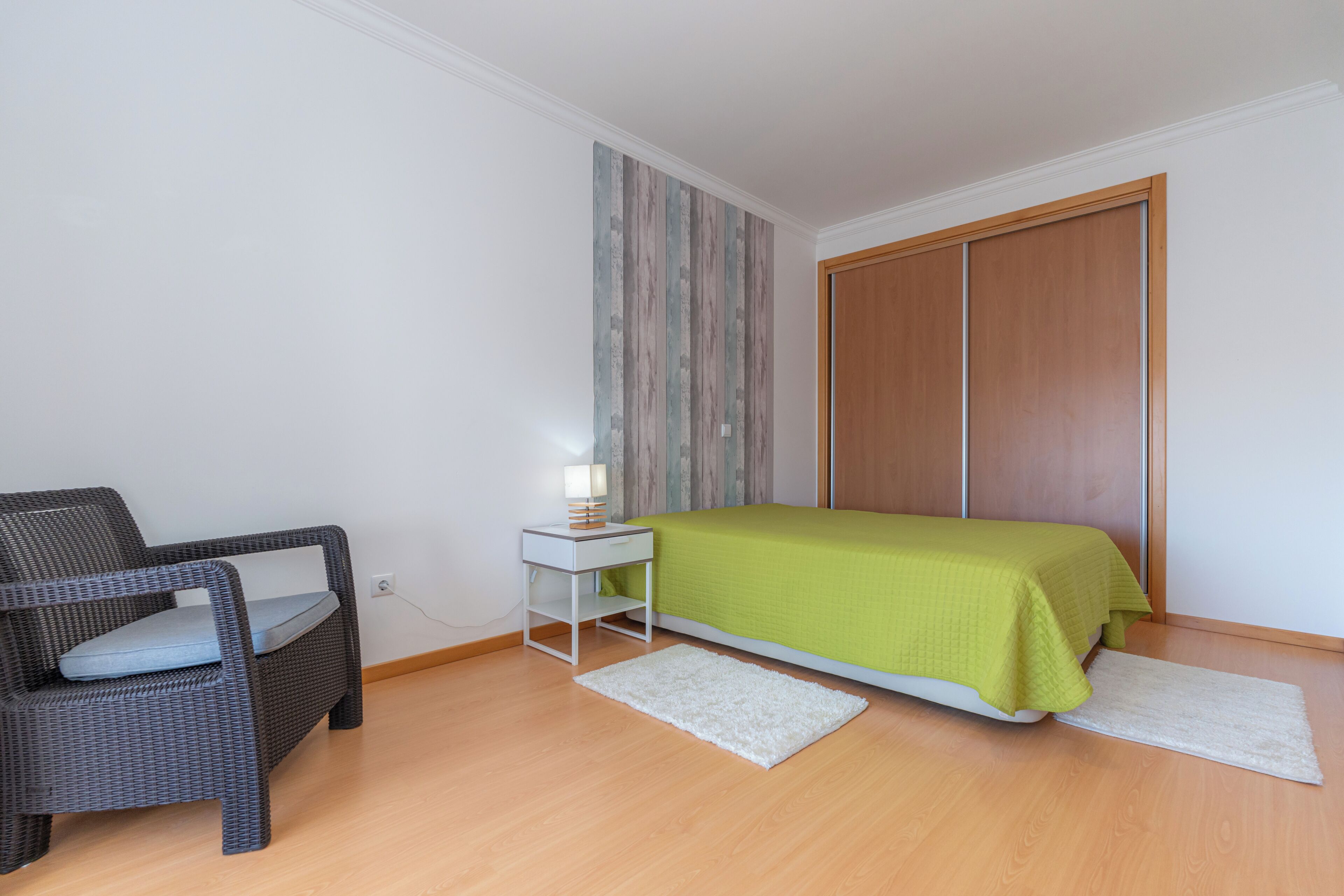 Een slaapkamer met een bed, een stoel, een nachtkastje en een wand met verticale strepen.