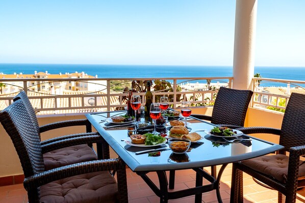 A dining table with chairs on a balcony overlooking the sea.