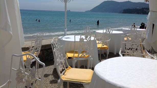 Outdoor seating with white chairs and tables, overlooking a beach with people swimming and a mountain in the background. - "MarViva" Air-conditioned house, 2/3 bedrooms - Private swimming pool, 5 min walk to the beach (La Seyne-Sur-Mer)