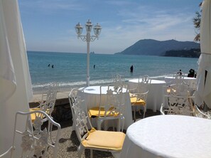 Outdoor seating with white chairs and tables, overlooking a beach with people swimming and a mountain in the background. - "MarViva" Air-conditioned house, 2/3 bedrooms - Private swimming pool, 5 min walk to the beach (La Seyne-Sur-Mer)