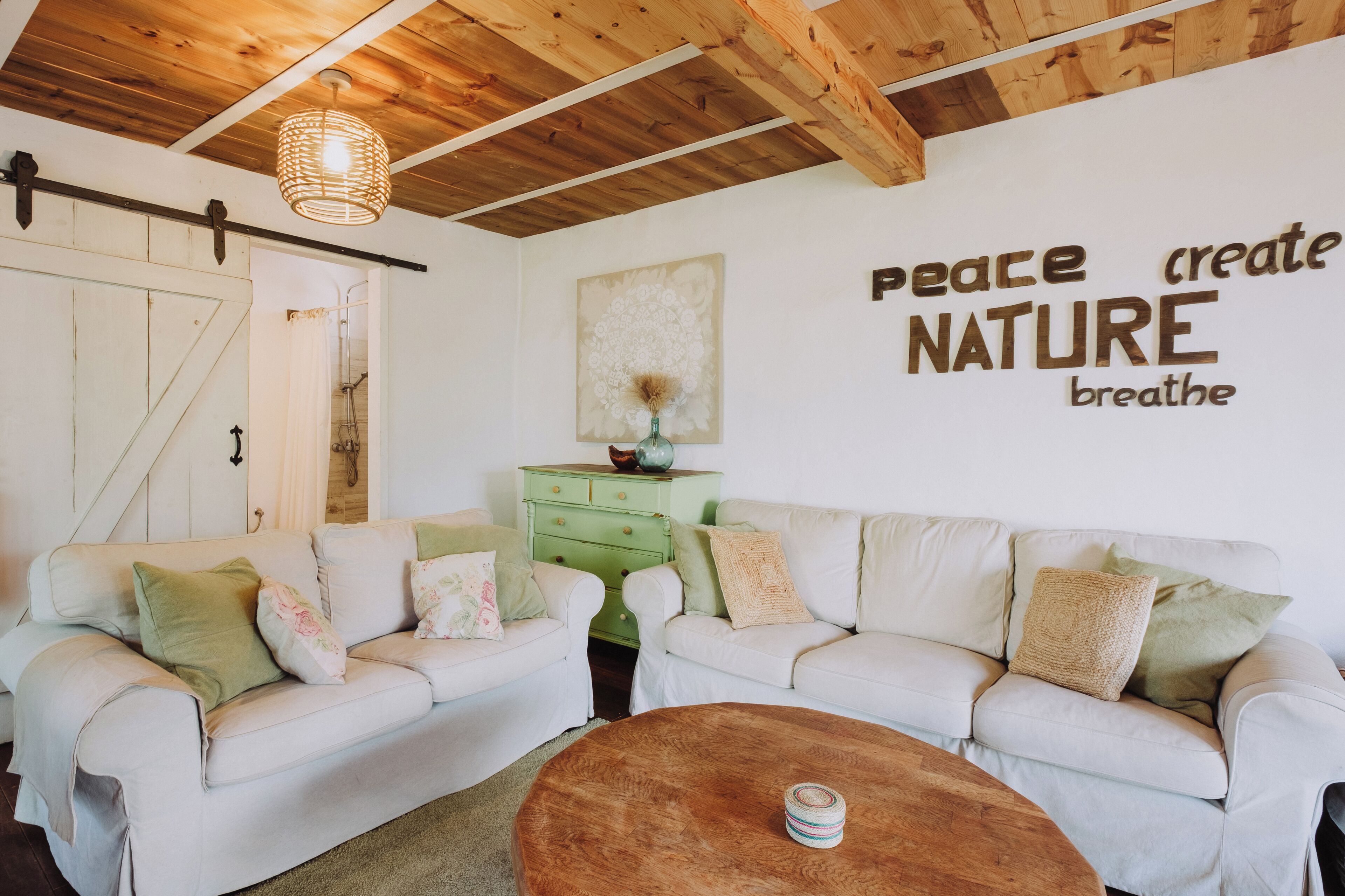 A room with two white sofas, a round wooden coffee table, a green dresser, and a wall with a nature-themed artwork.