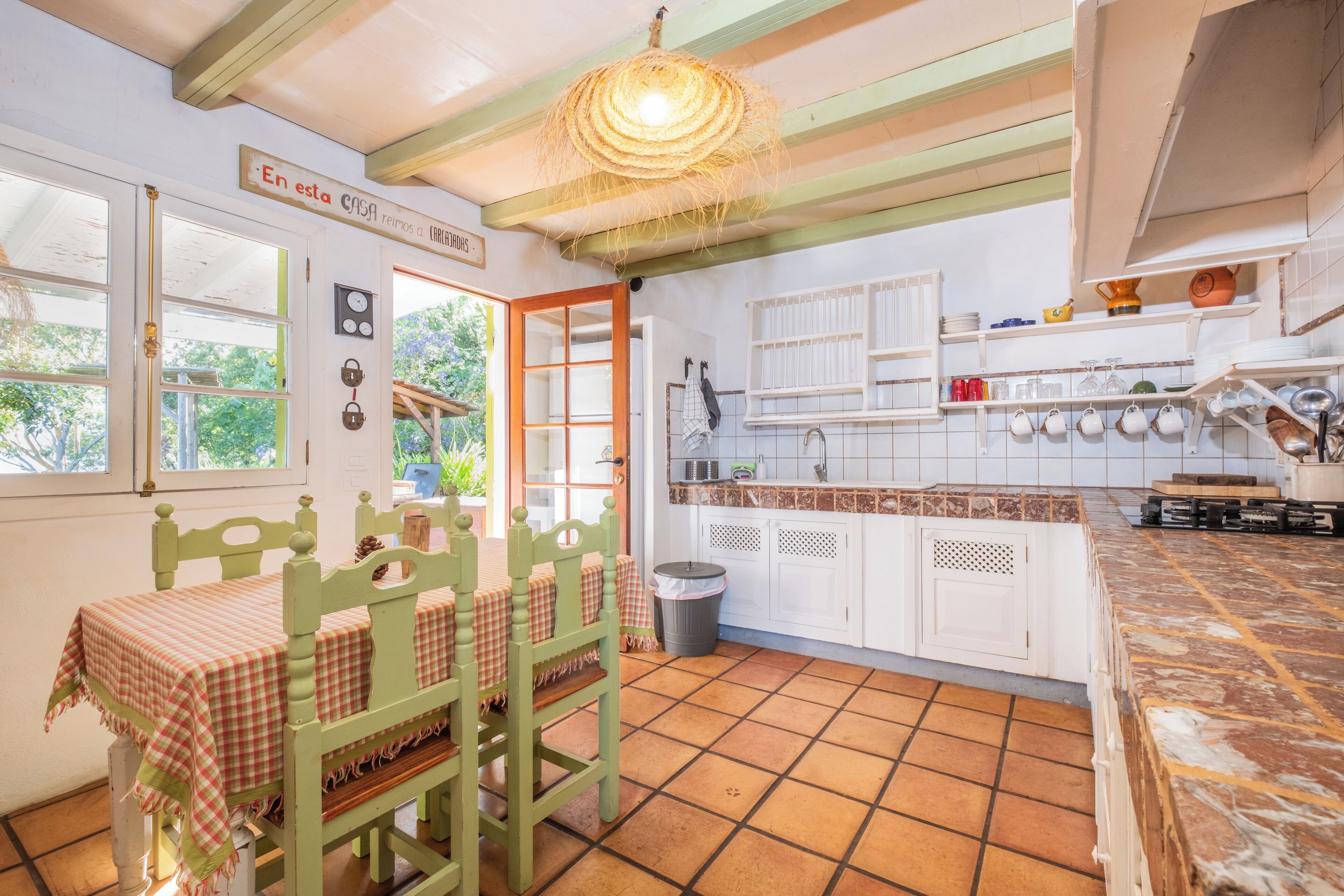 Eine Küche mit einem grünen Tisch und Stühlen, weißen Schränken und einer an der Decke befestigten Küchenutensilienstange.