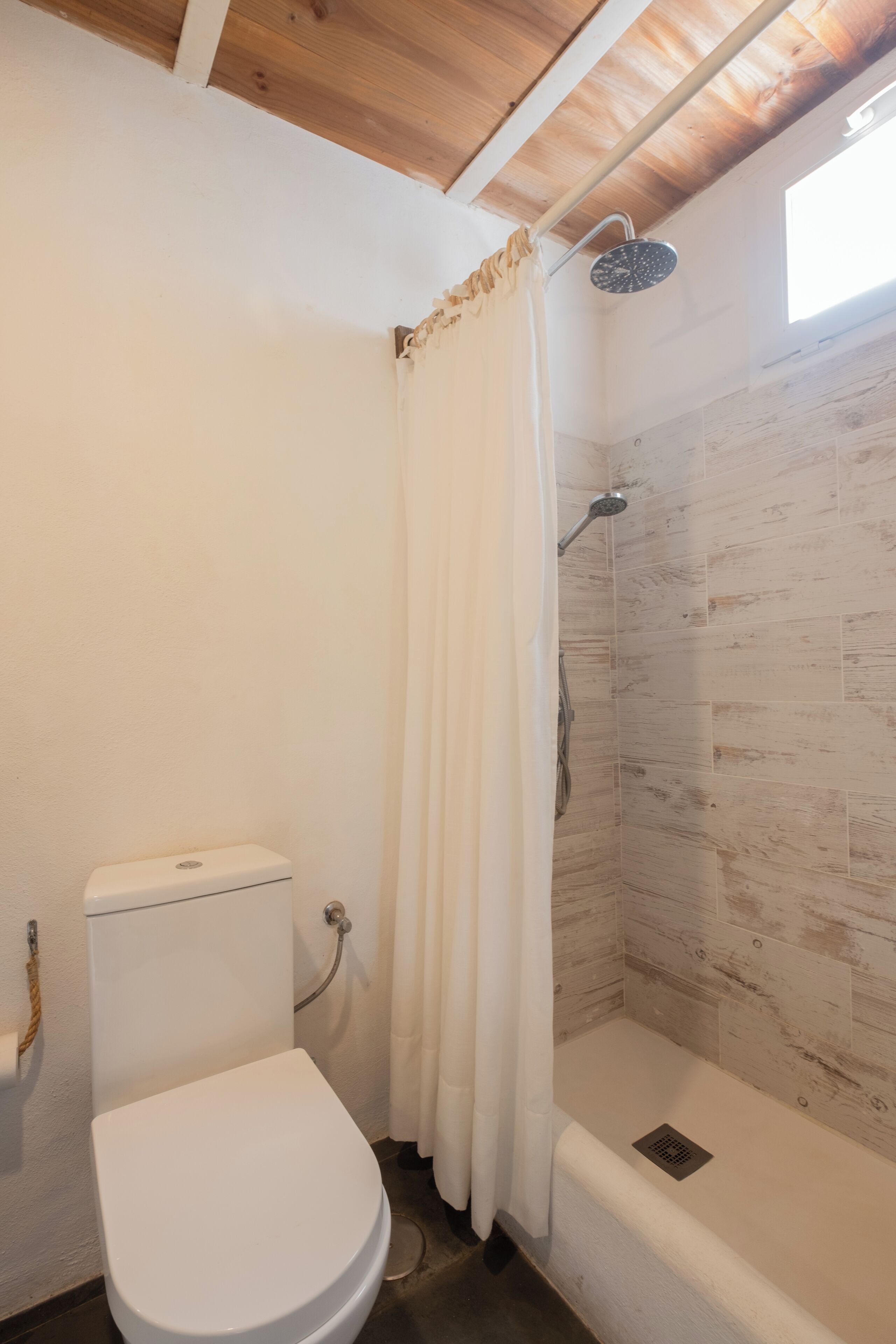 A bathroom with a shower, toilet, and a window.