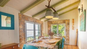 A dining area with a stone wall, wooden ceiling beams, a table set with plates and candles, and chairs.