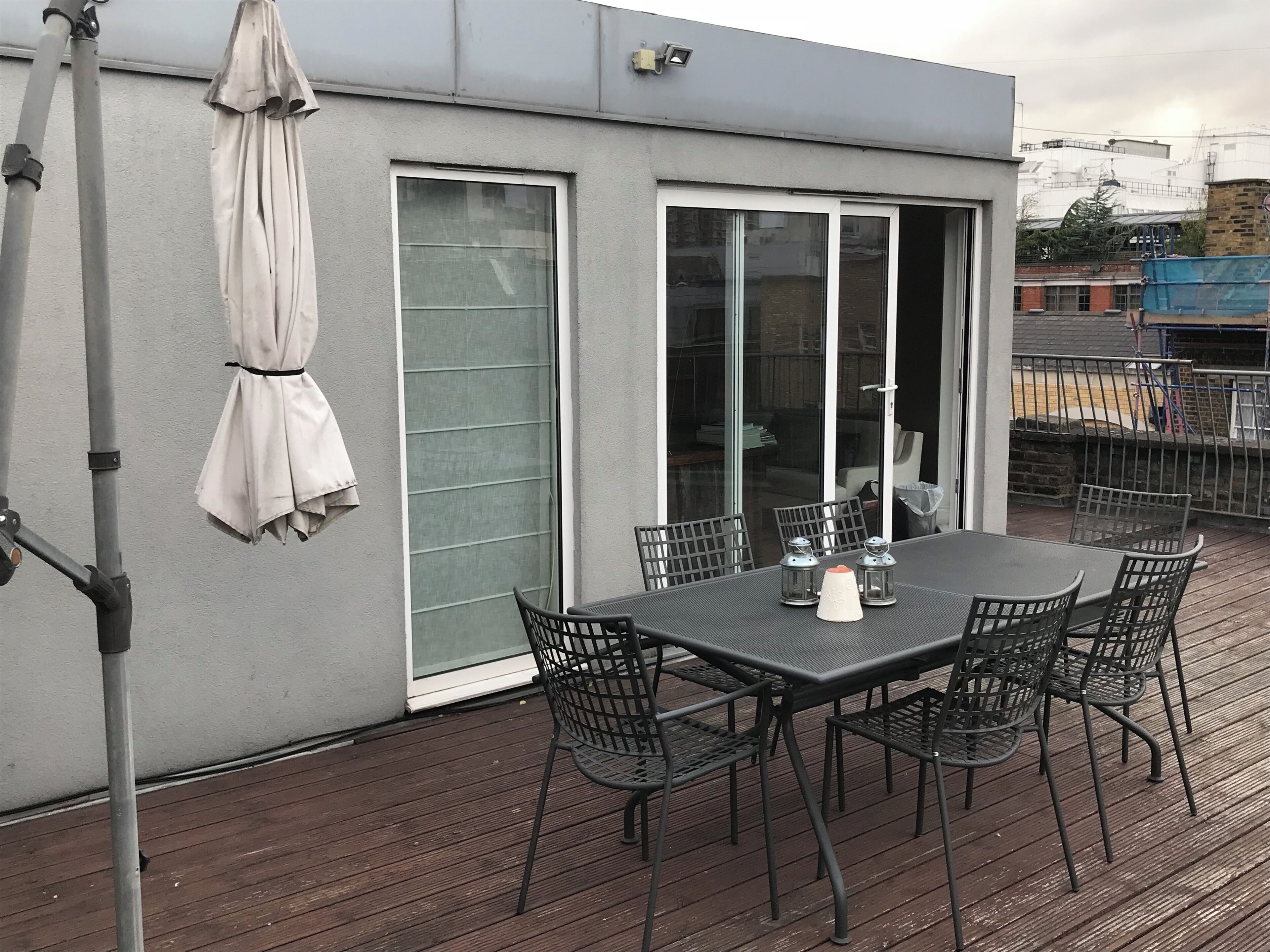 A balcony with a table and chairs, a covered umbrella, and a sliding glass door.
