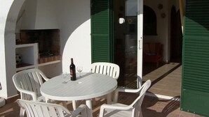 Un patio al aire libre con una mesa redonda y sillas, una botella de vino y un horno de ladrillo.