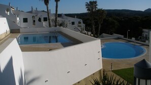 Zona de piscina con un edificio blanco y palmeras.
