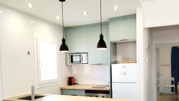 Una cocina moderna con una isla central, iluminación colgante y un microondas.