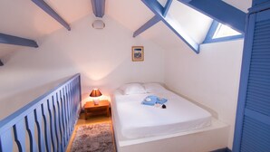 Un dormitorio con techo inclinado, una cama con ropa de cama blanca, una mesita de noche con lámpara y una alfombra pequeña.