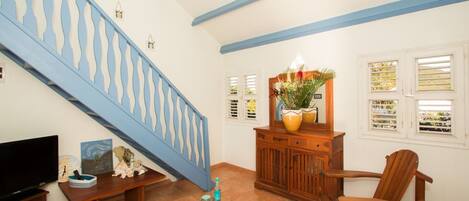 A living room with a blue staircase, a wooden cabinet with a mirror, a television, and a plant.