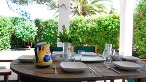 Une table dressée à l’extérieur, avec des assiettes, des couverts et une carafe.