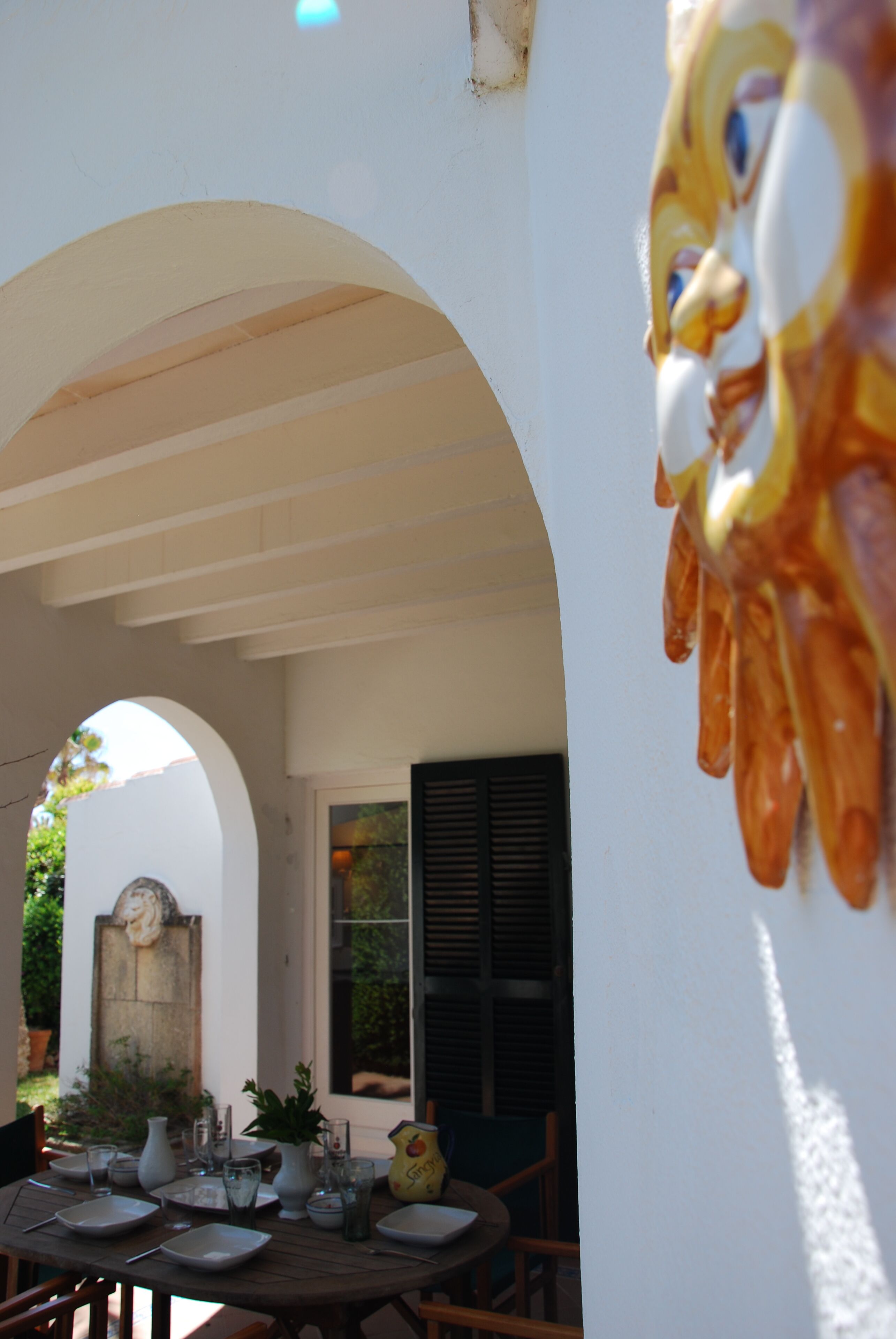 An outdoor dining area with a white wall, an archway, and a table set for two.