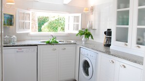 Une cuisine équipée d’un lave-vaisselle, d’un lave-linge, d’un évier et d’une fenêtre donnant sur un espace verdoyant.