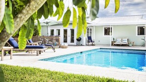 A swimming pool with lounge chairs and a house in the background.