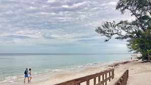 A beach with a wooden boardwalk, clear skies, and calm water.