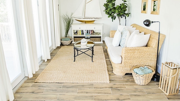 A living room with a wicker sofa, a ceiling fan, a bookshelf, and a large window with curtains.